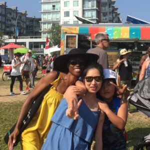 Two racialized women and a child sming at an outdoor festival