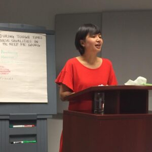 Racialized woman in a red dress speaking at a podium